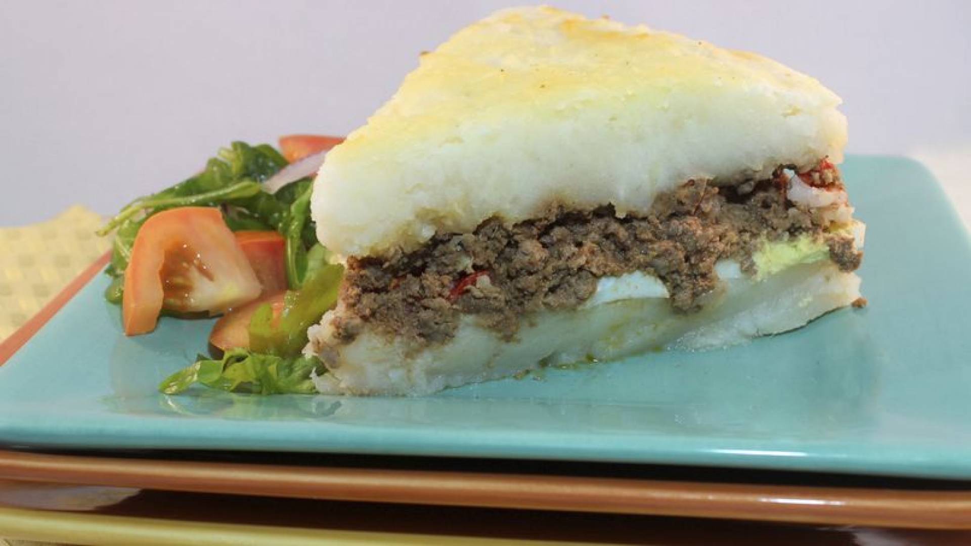 Pastelon de viandas relleno de pollo guisado acompanado con ensalada de pepinillos y tomates